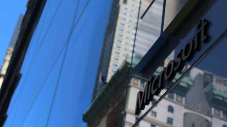 A Microsoft logo on a glass wall witha reflection of a blue sky