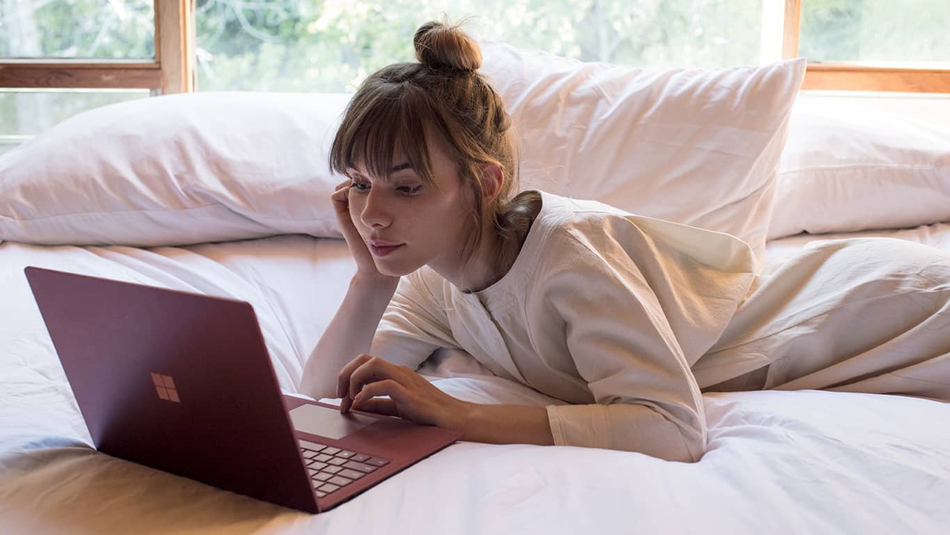 Woman reading email on a Surface on bed
