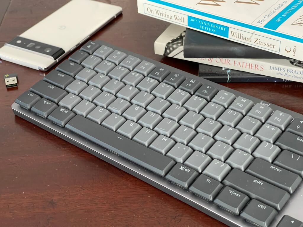 The Logitech MX Mechnical sitting on a desk next to a phone and books.